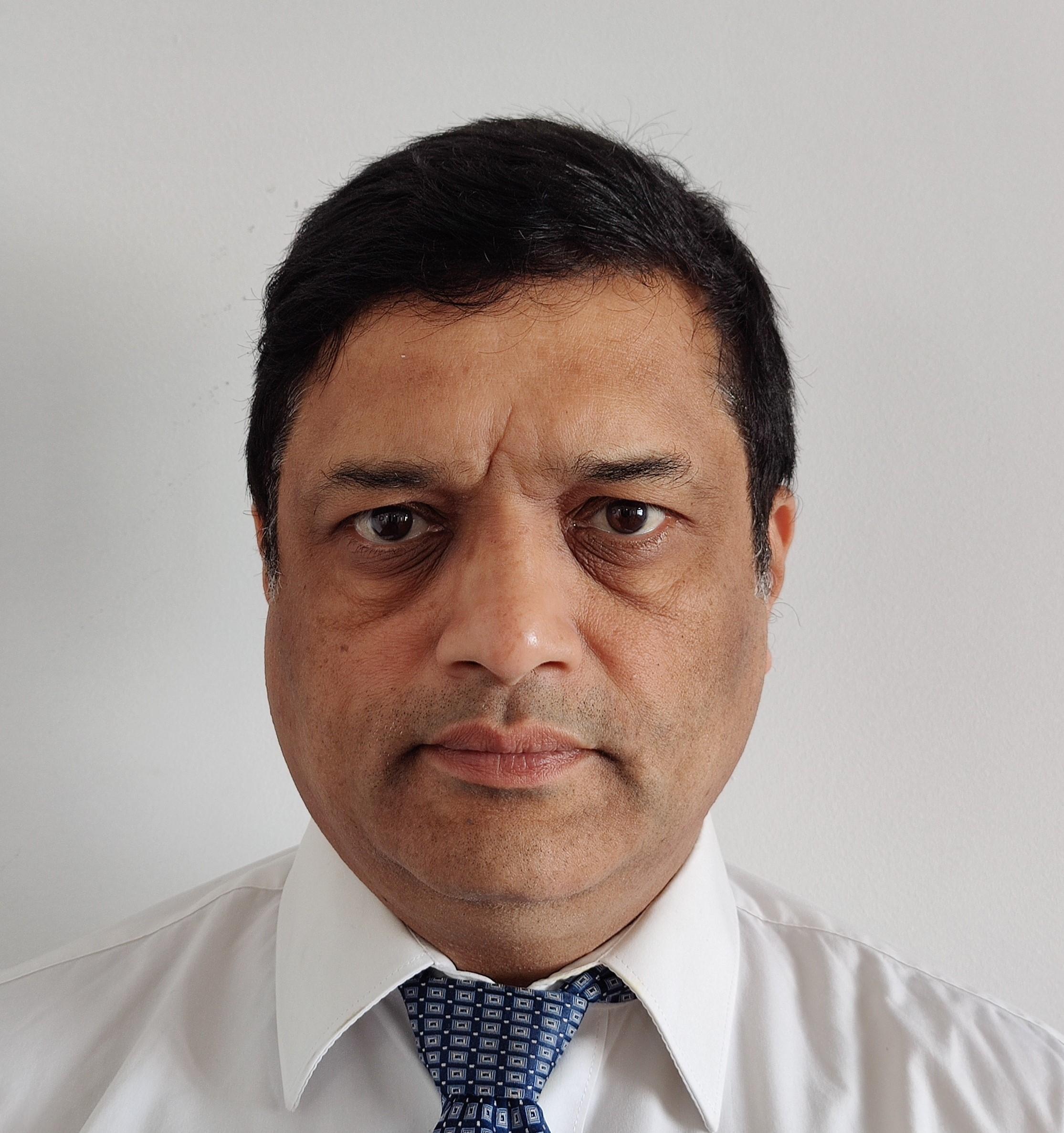 A middle-aged man with short dark hair wears a white shirt and patterned blue tie, looking directly at the camera with a neutral expression, against a plain white background—perfect for professional use at Indo Intertex events.