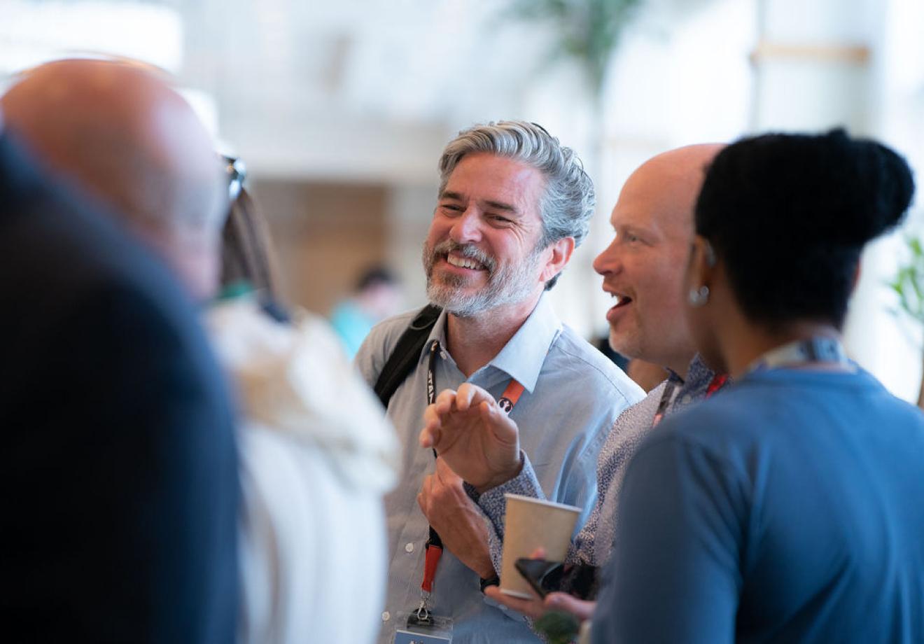 we-are-1 Professionals engaged in animated conversation at a networking event, with one holding a coffee cup in a bright venue.
