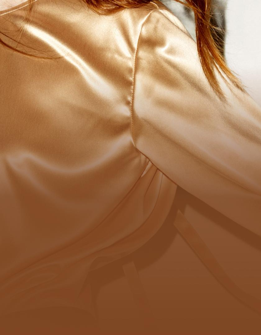 NinaRicci Close-up of a silky champagne-colored blouse or garment with visible seams and a glimpse of auburn hair.